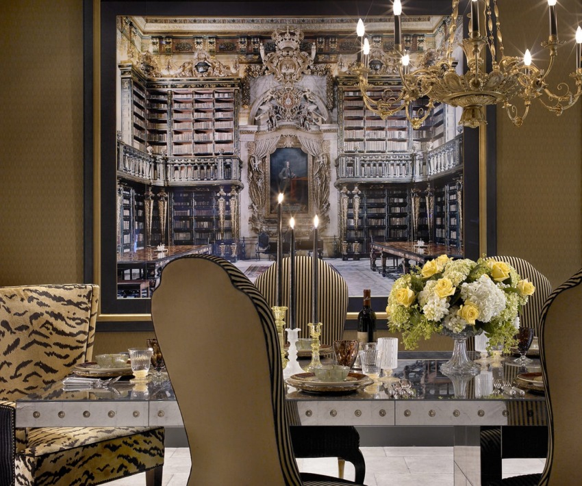 Elegant dining room with a decorated table and chandelier, featuring a large antique library mural as a backdrop.