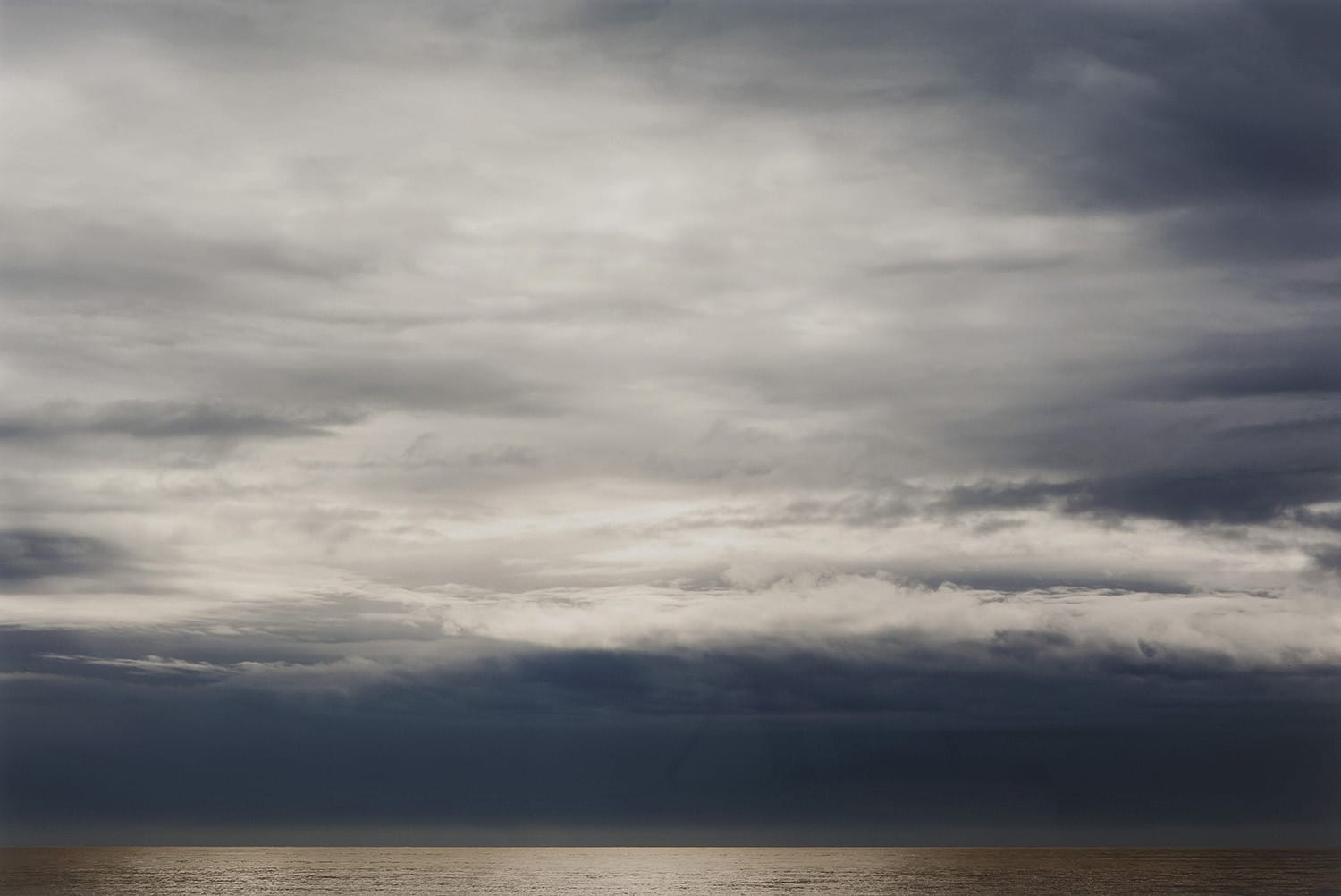 Dramatic cloudy sky over a calm ocean with subtle sunlight reflecting on the water surface.