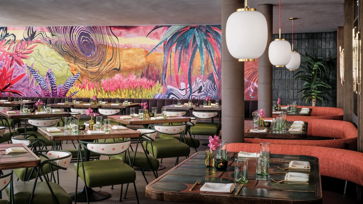 Colorful restaurant interior with vibrant mural, elegant lighting, and neatly set tables, evoking a lively and inviting atmosphere.