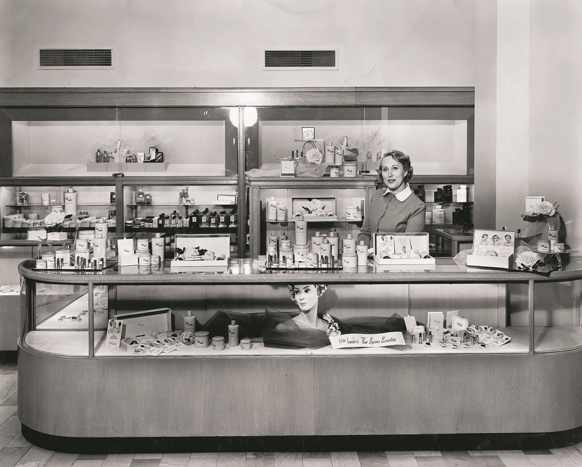 Vintage photo of a woman behind a makeup counter in a department store with various products on display.