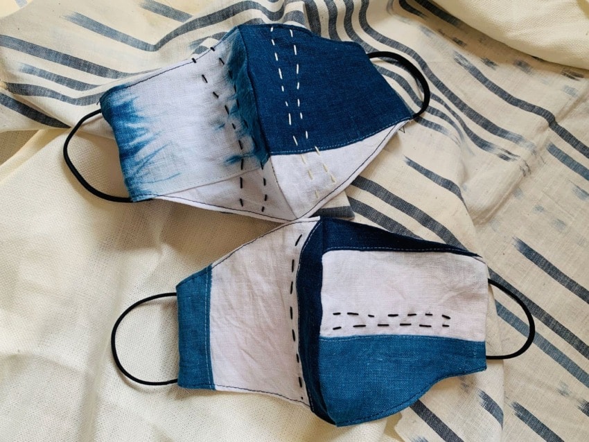 Two handmade masks with blue and white patchwork design on a striped fabric background.