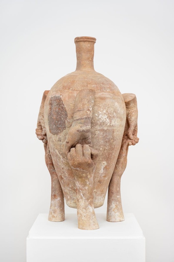 Ancient terracotta artifact with multiple legs and handles displayed on a white pedestal in a museum setting.