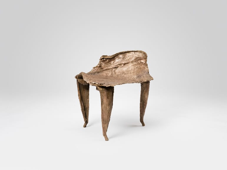 Sculptural bronze chair with organic, uneven surfaces and three tapered legs against a plain background.