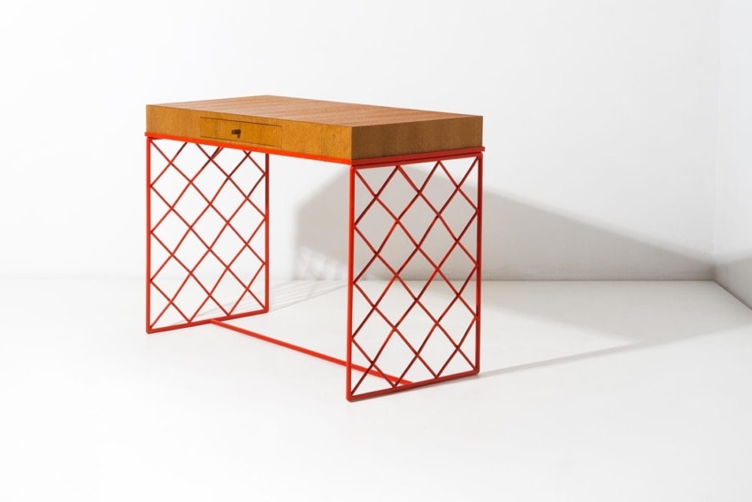 Modern desk with a wooden top and vibrant red lattice legs against a white background.