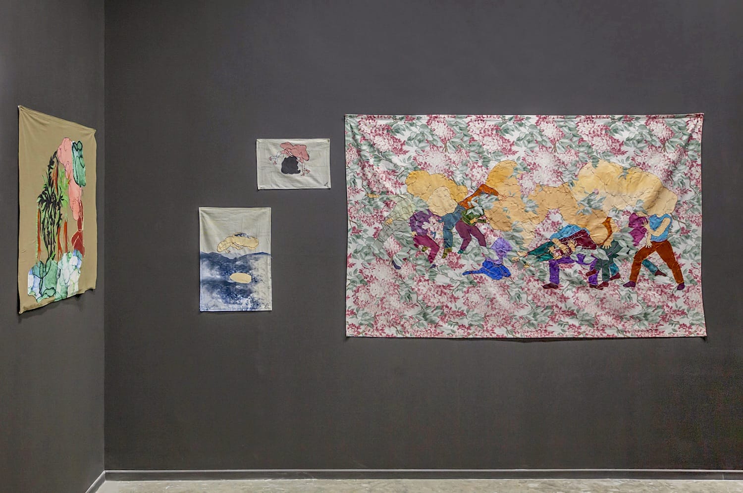 Art gallery wall displaying diverse textile and fabric artworks with floral patterns and abstract designs.
