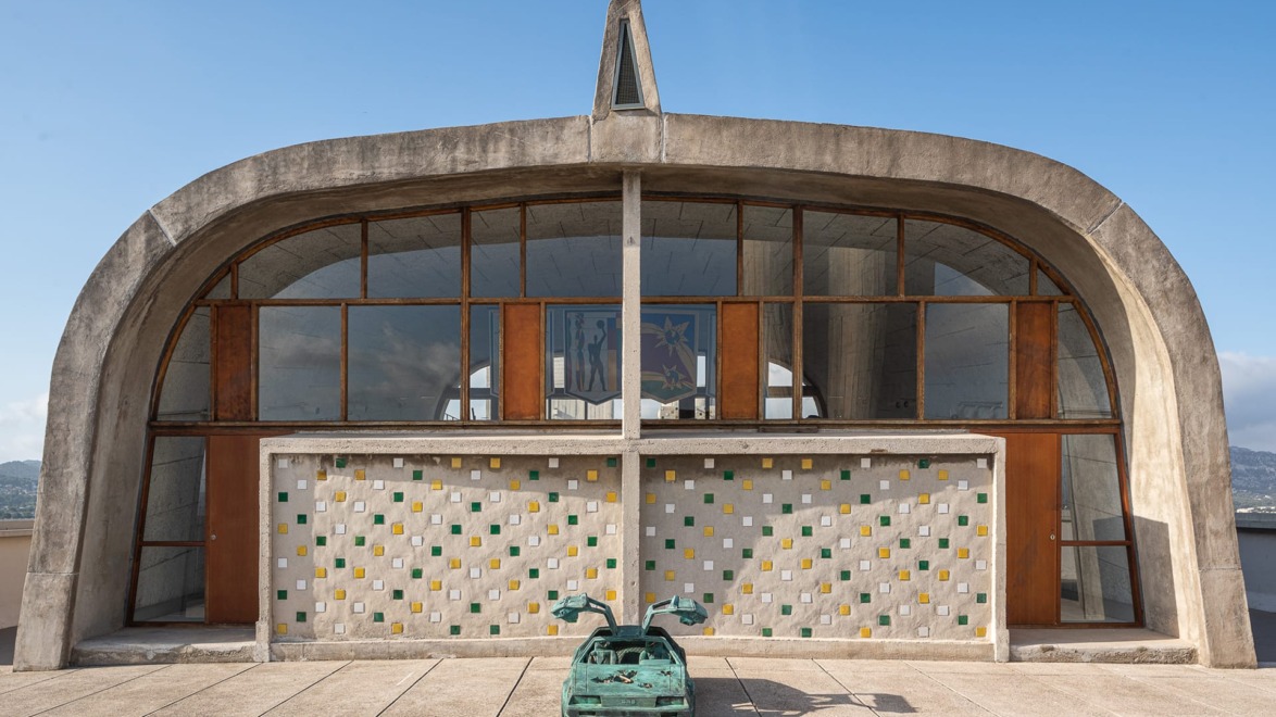 Modernist church facade with colorful tile wall and a turquoise sculpture in front under a clear blue sky.