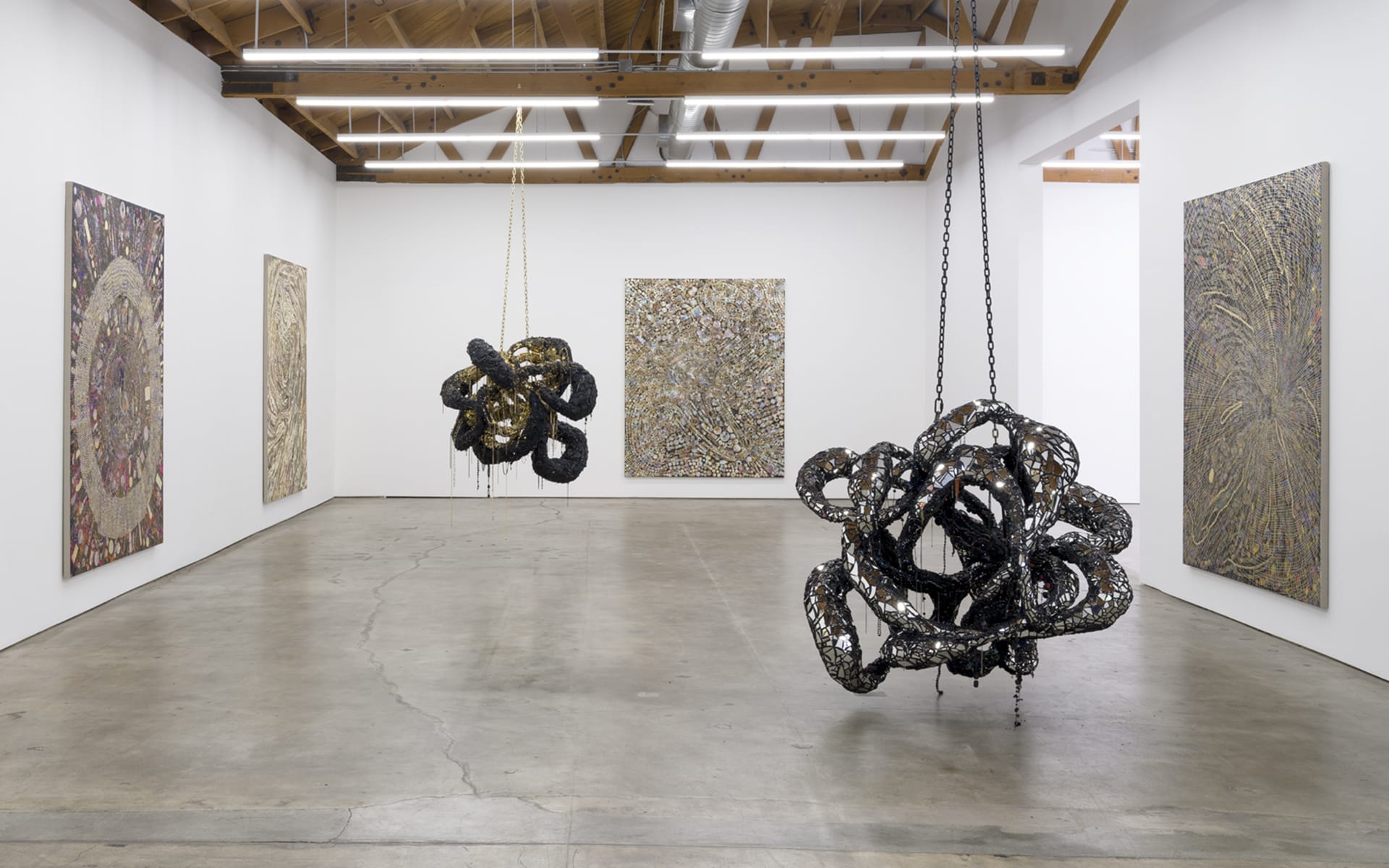 Art gallery with abstract sculptures hanging from the ceiling and textured paintings on white walls.