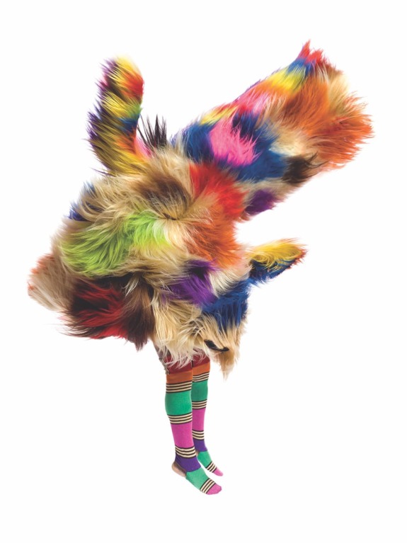 Person in colorful fur costume and striped socks standing on one leg against a white background.