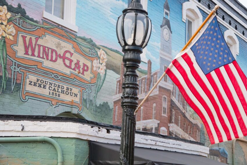 Mural of Wind Gap town sign and American flag on brick building wall with historical imagery and vintage design.
