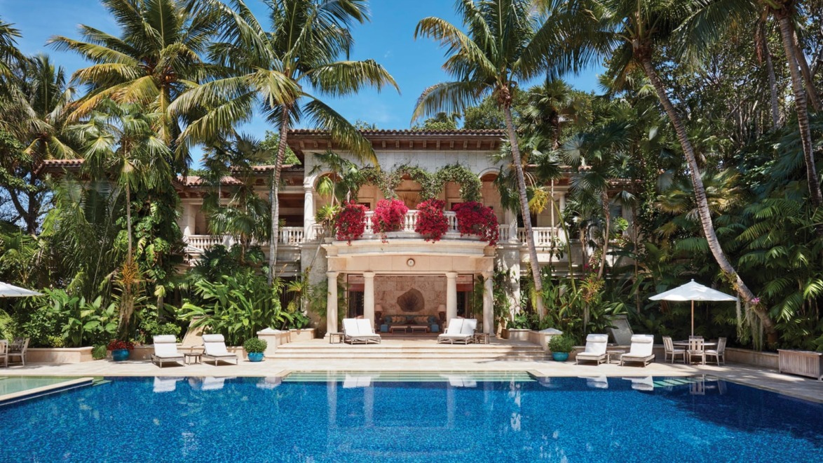 Luxurious tropical villa with a large pool, surrounded by palm trees and lush greenery, featuring elegant architecture.