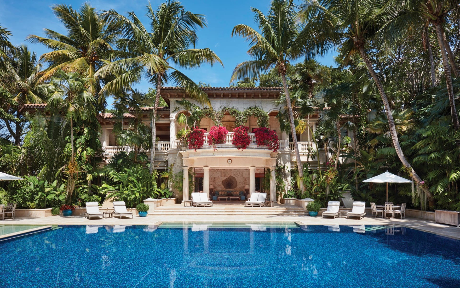 Luxurious tropical villa with a large pool, surrounded by palm trees and lush greenery, featuring elegant architecture.