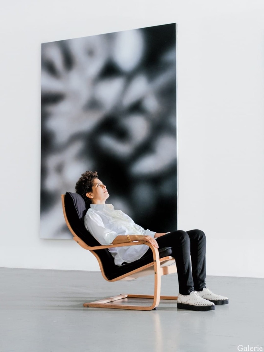 Person relaxing in a modern chair inside an art gallery with a large abstract painting in the background.