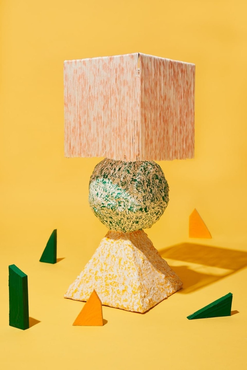 Colorful abstract lamp with square shade and pyramid base against a yellow background with scattered geometric shapes.