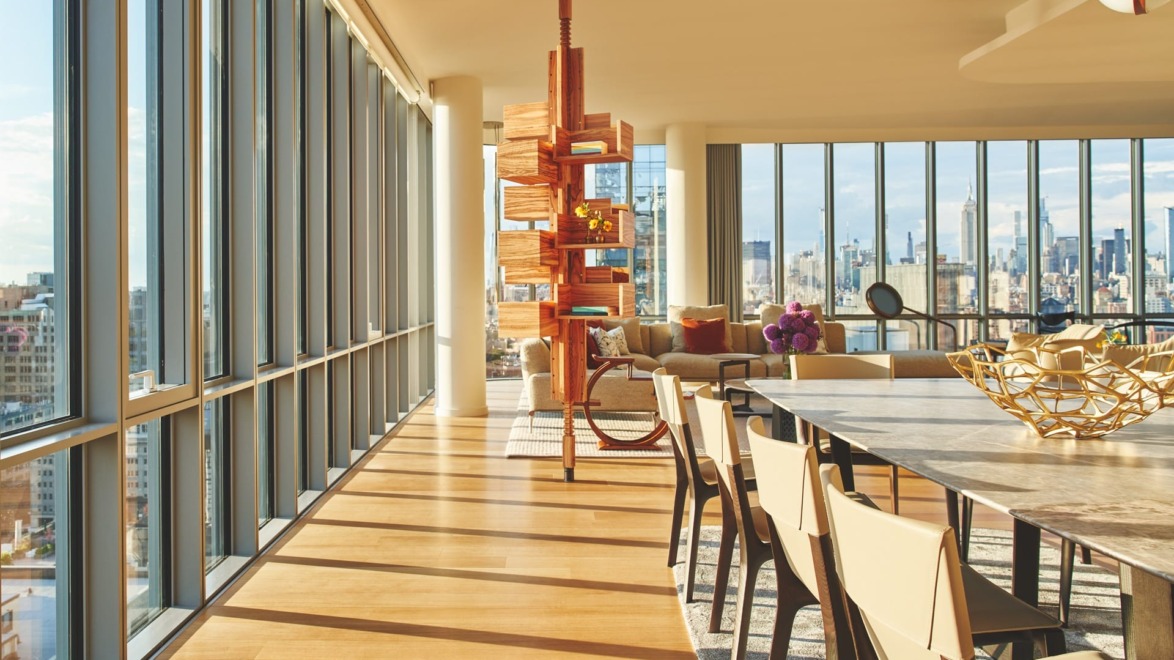 Bright modern apartment with floor-to-ceiling windows, city skyline view, wooden dining table, chairs, and contemporary decor.