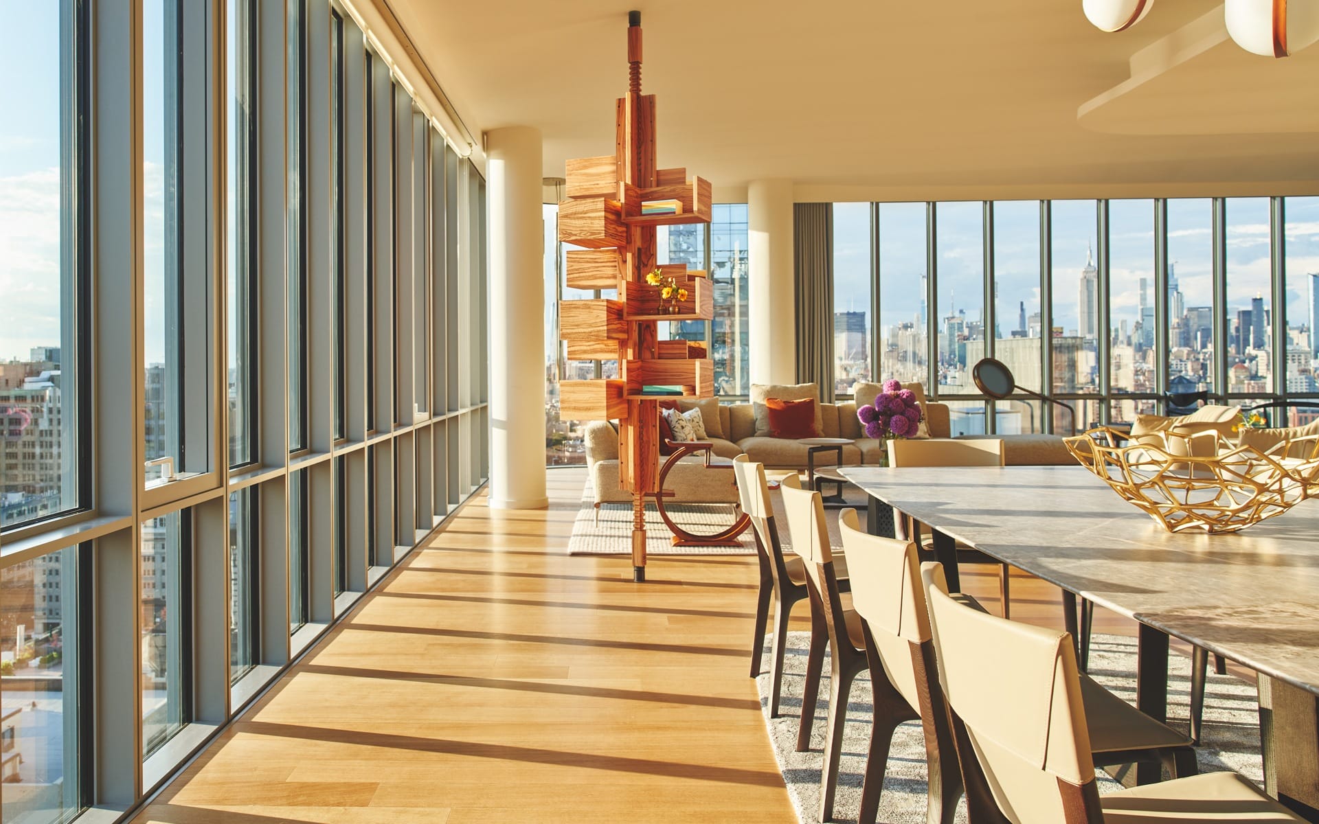 Bright modern apartment with floor-to-ceiling windows, city skyline view, wooden dining table, chairs, and contemporary decor.