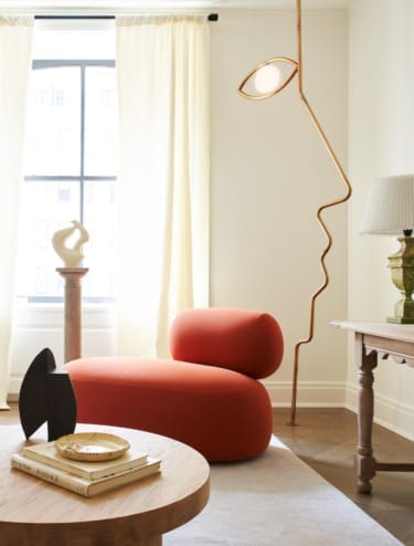 Modern living room with a curved red chaise lounge, abstract floor lamp, and contemporary decor in natural light.