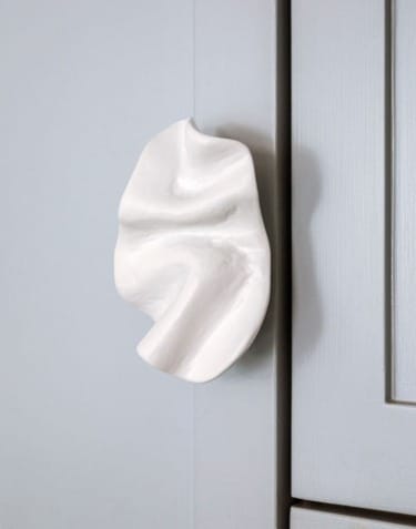 Abstract white ceramic sculpture on a blue-gray wall.