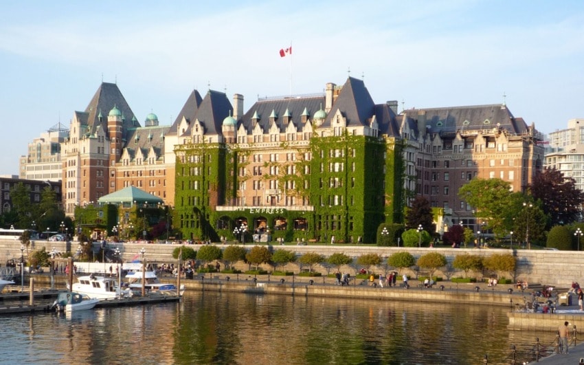 Ivy-covered historic hotel by waterfront under clear skies with boats docked in foreground and lush greenery around building