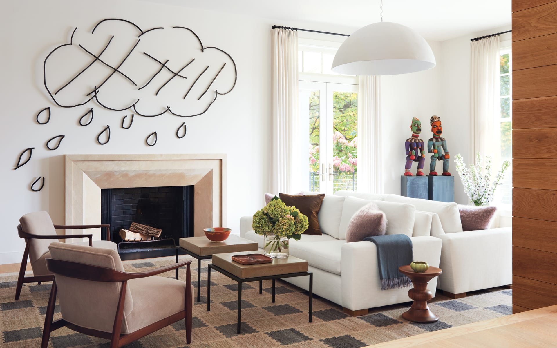 Modern living room with white sofa, artistic wall decor, natural light, and eclectic sculptures on display.
