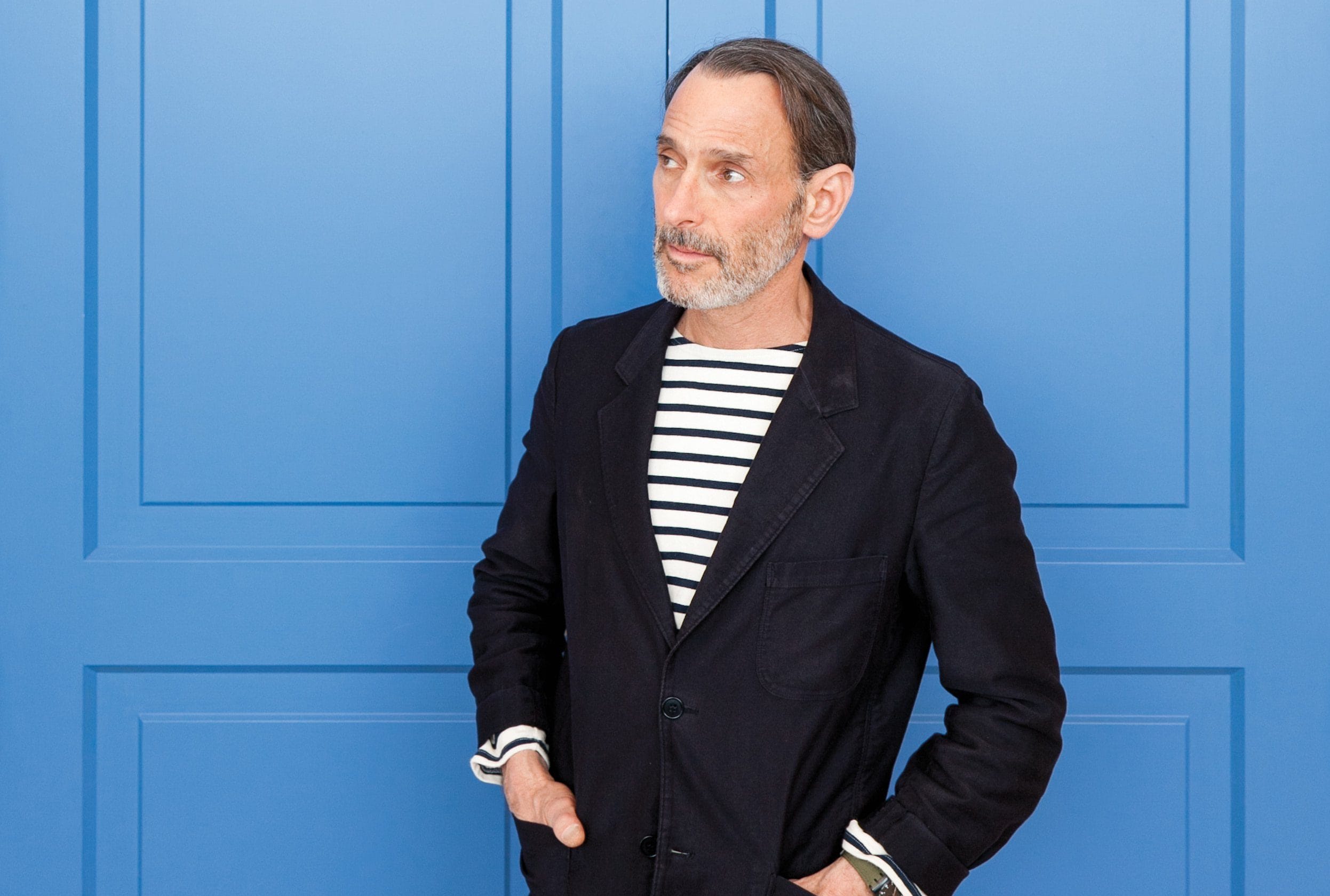Man in striped shirt and dark blazer posing against a blue background