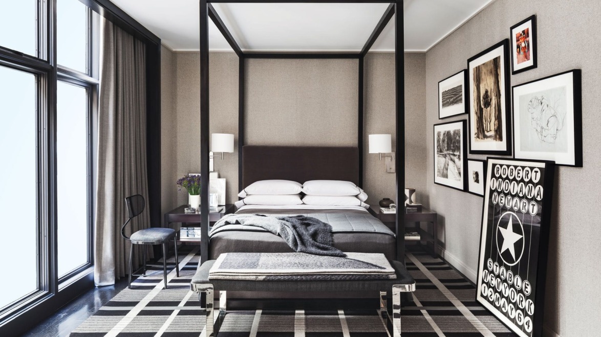 Elegant modern bedroom with a four-poster bed, stylish artwork on walls, large windows, and patterned rug.