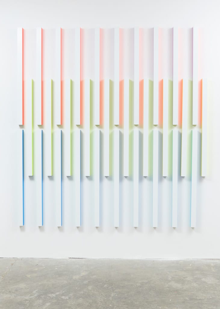 Colorful abstract wall art with vertical gradient stripes in pink, green, blue, and white on a plain background.
