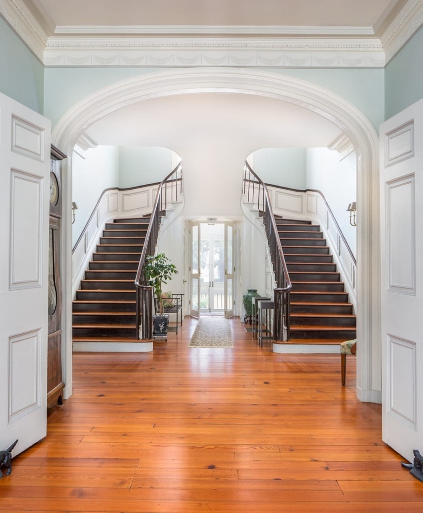 Elegant foyer with dual wooden staircases, arched entryway, polished wood floor, and large windows for natural light.