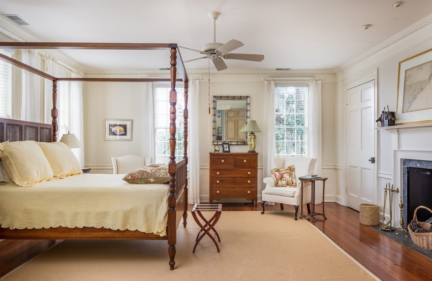 Elegant bedroom with a four-poster bed, wooden floor, cozy seating, and a fireplace, decorated in neutral tones.