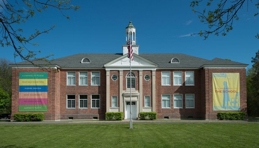 Red brick building with white columns, a central cupola, an American flag, and colorful banners on the front facade.