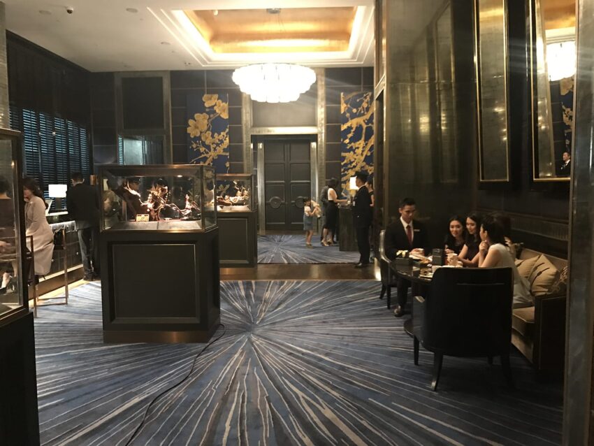 People in a luxurious lounge with a blue carpet, decorative wall panels, and a chandelier overhead.