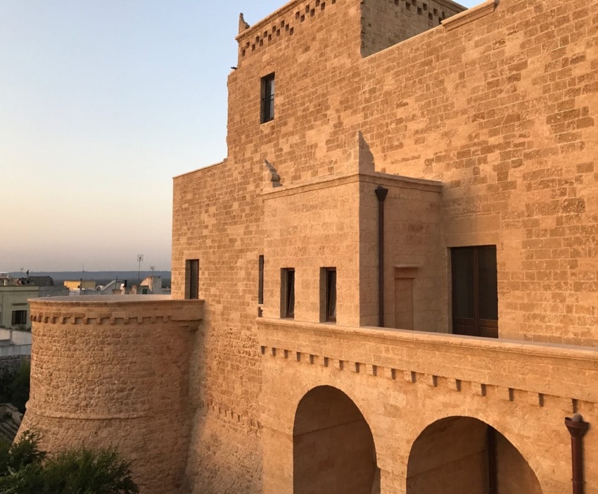 Ancient stone fortress with arches and tower, bathed in warm sunlight against a clear sky.