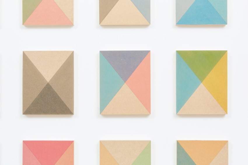 Colorful geometric patterns in pastel shades on wooden panels arranged in a grid on a white background.