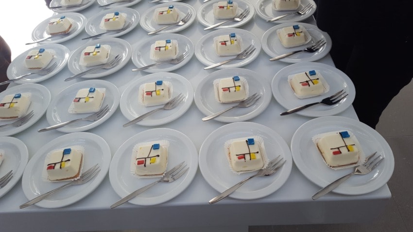 Plates of white cakes decorated with geometric patterns in red, blue, yellow, and black on a table.