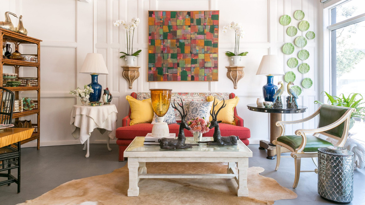 Eclectic living room with colorful art, red sofa, various decorative items, plants, and a mix of furniture styles.