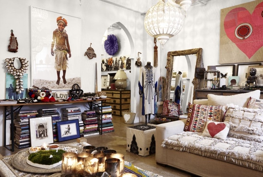 Bohemian-style living room with eclectic decor, large wall art, patterned cushions, and shelves filled with books and collectibles.