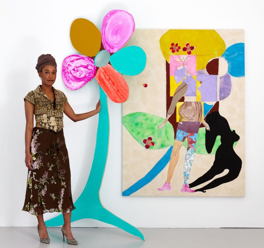 Woman standing beside a colorful abstract painting and a large flower art piece in an art gallery.