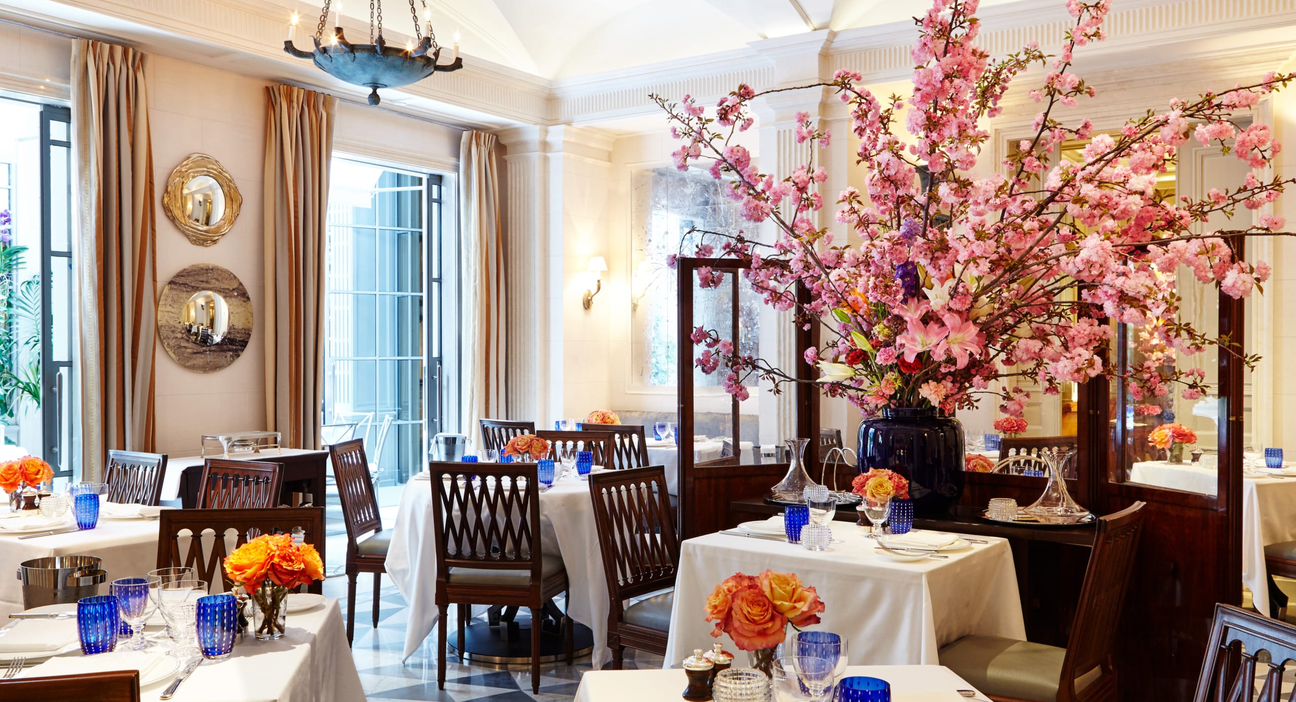 Elegant restaurant interior with cherry blossom centerpiece, set tables, and wooden chairs under a high ceiling.