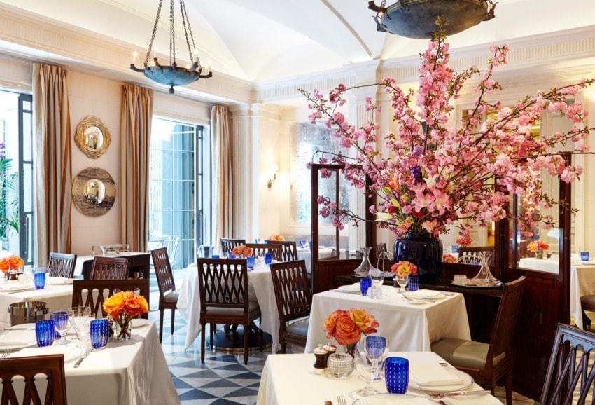 Elegant restaurant interior with cherry blossom centerpiece, white tablecloths, blue glasses, and orange flower arrangements.