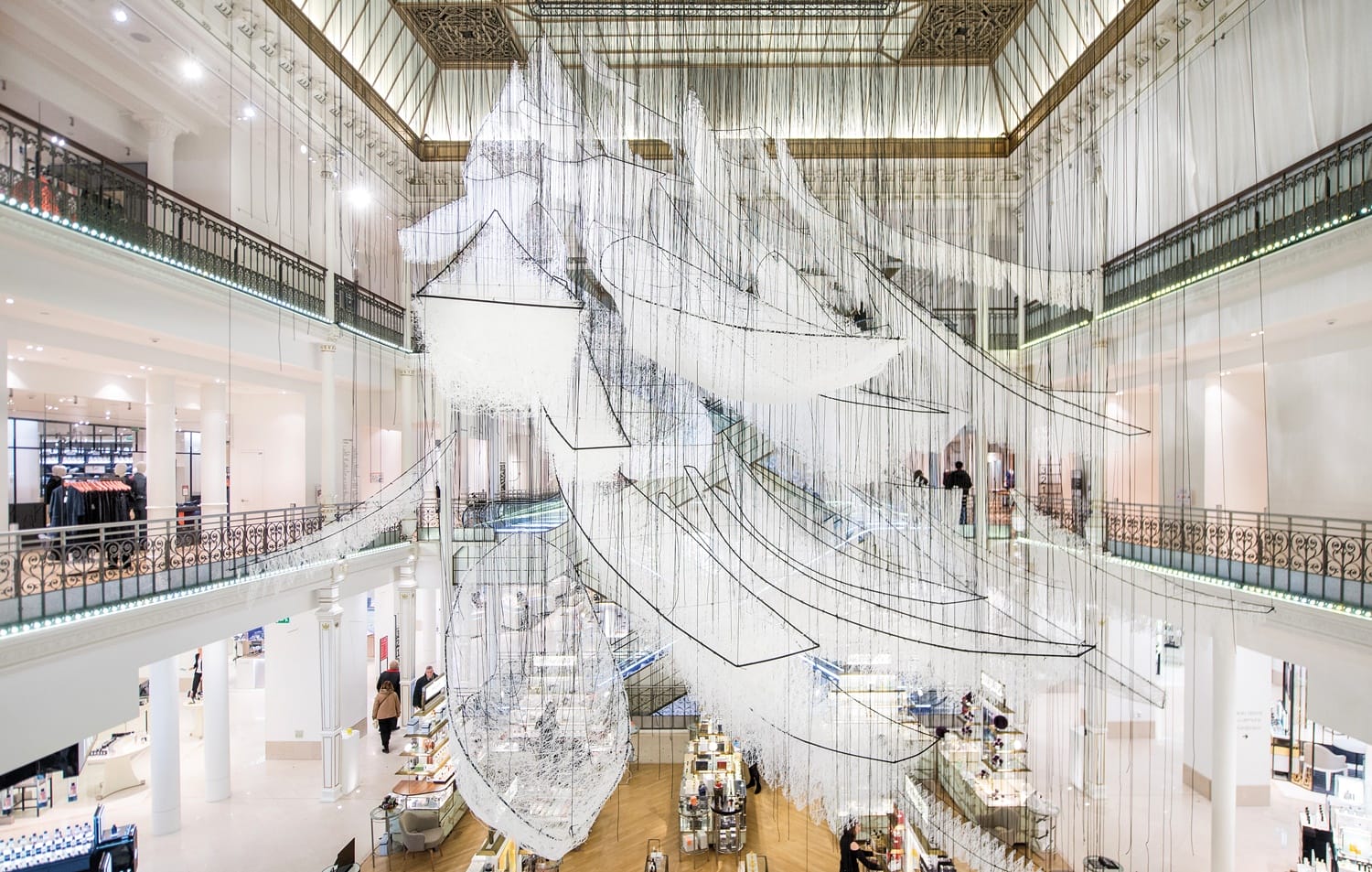Intricate hanging art installation in a spacious, modern store interior with multiple floors and decorative railings.