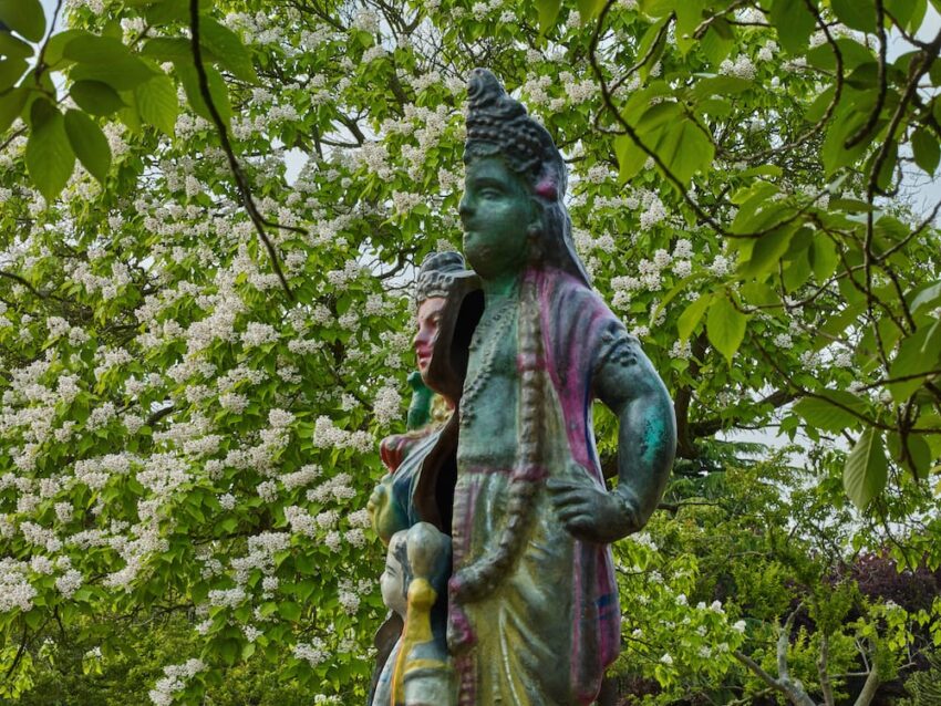 statues of a couple surrounded by lush green leaves and white flowers in a park or garden setting