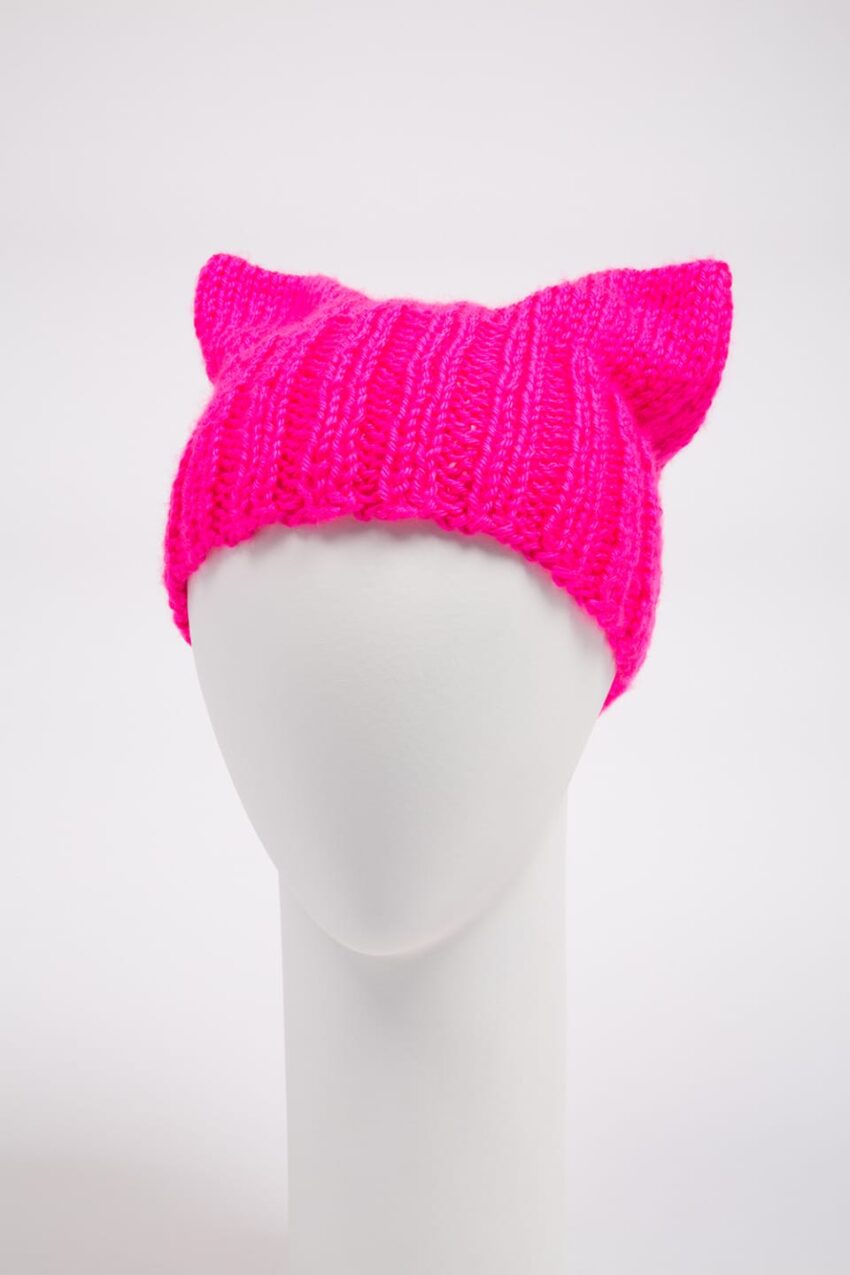 Bright pink knitted hat with cat ears on a mannequin head against a plain background.