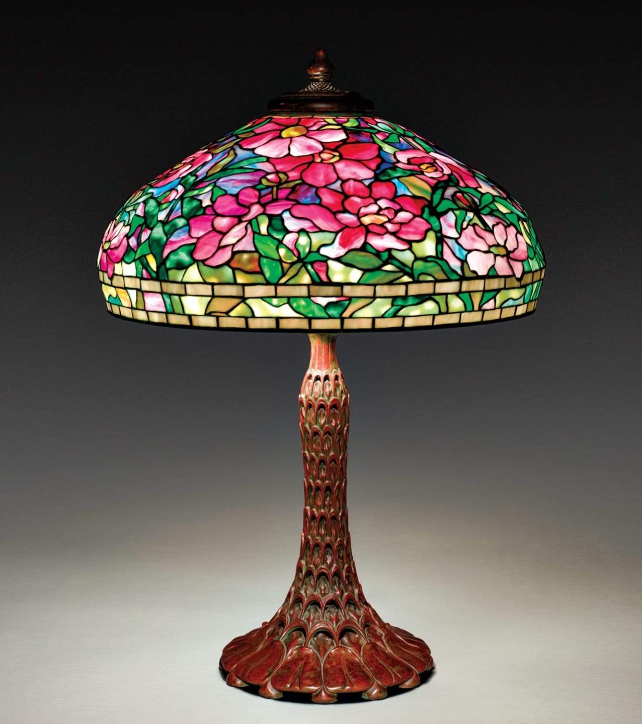 Colorful floral stained glass Tiffany-style lamp with intricate design and detailed bronze base on a dark background.