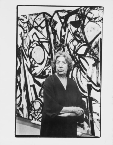 Woman standing in front of a large abstract painting with bold black and white patterns.