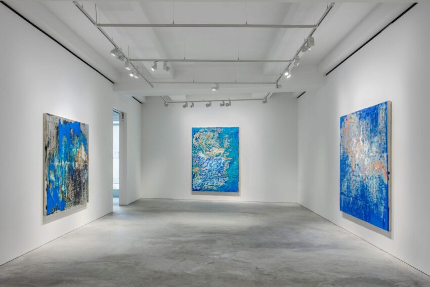 Art gallery with abstract blue paintings on white walls and track lighting.