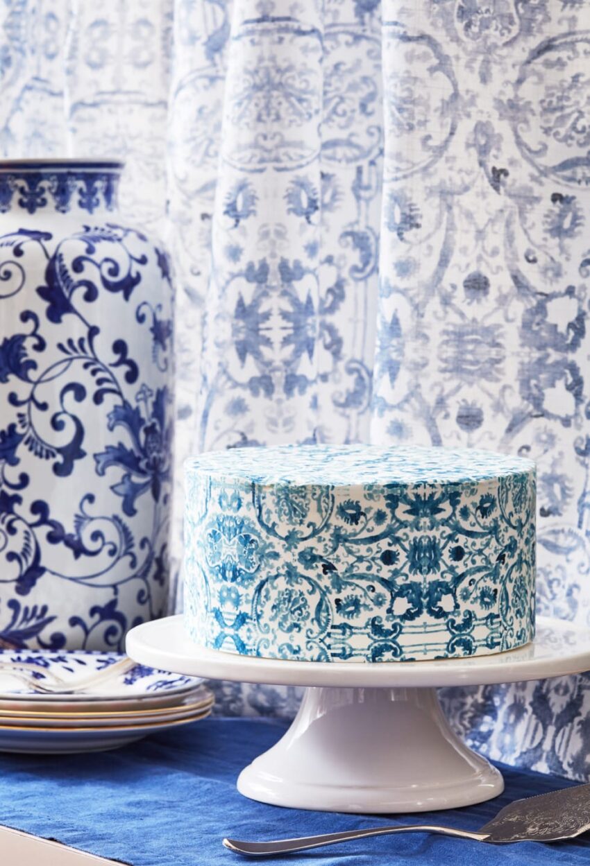 Blue and white patterned cake on a white stand next to a large decorative vase with a similar design.