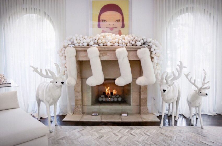 Elegant living room with a lit fireplace, white stockings, modern art, and decorative reindeer figures for Christmas.