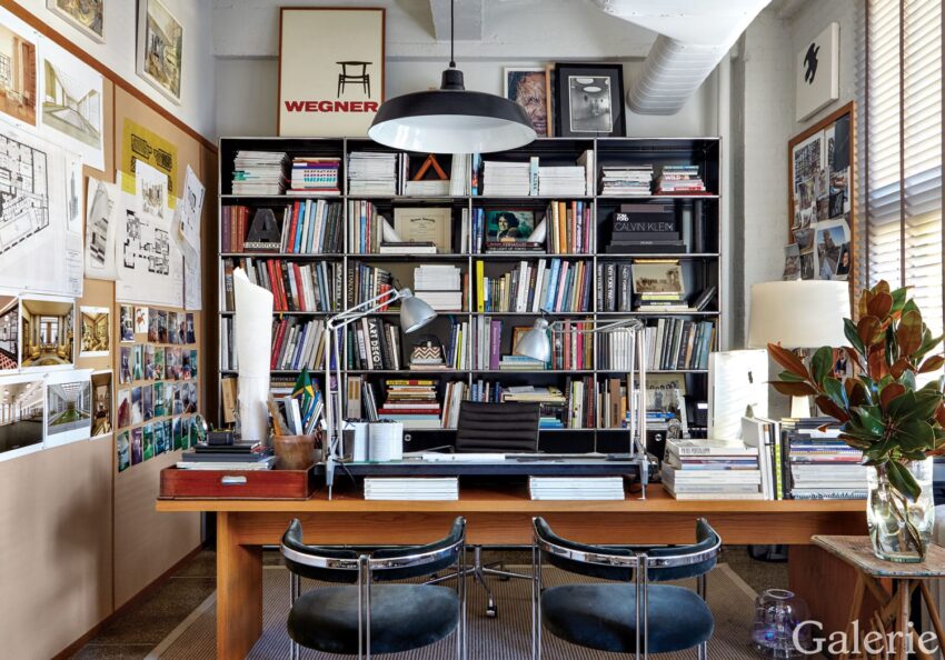 Modern office with a large bookshelf, desk with two lamps, chairs, and wall art, creating a cozy and organized workspace.