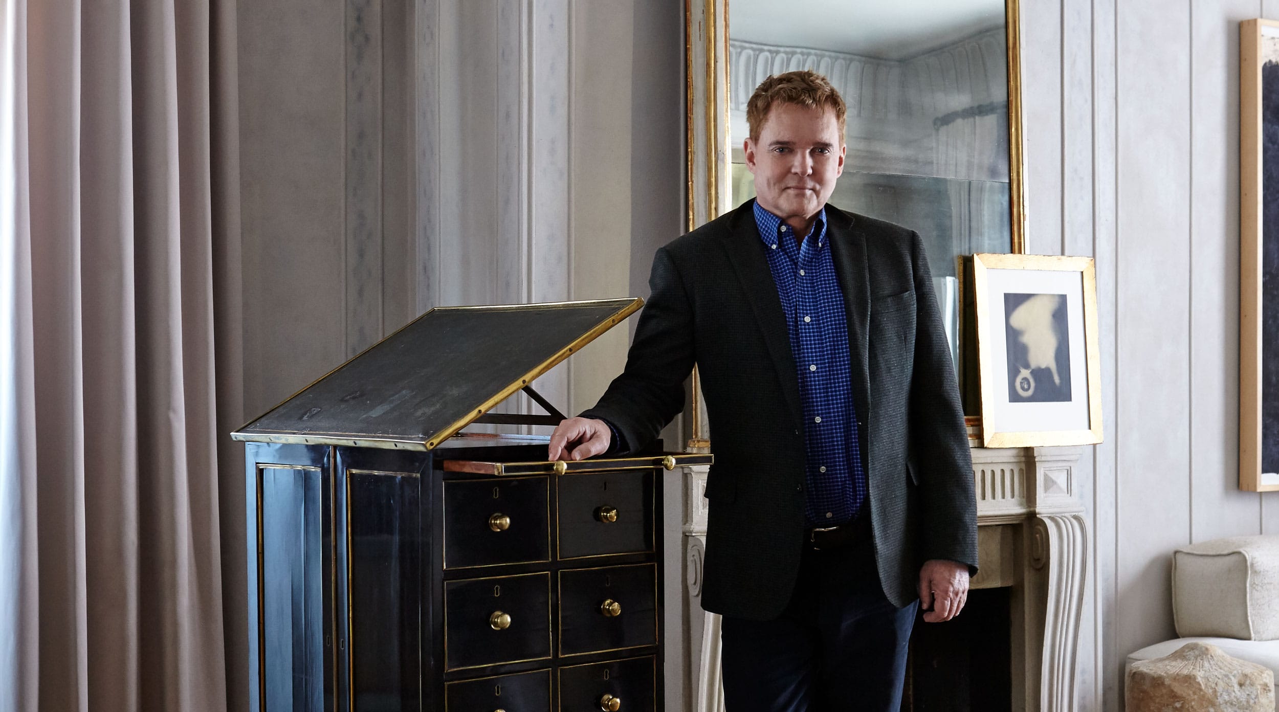 Man standing next to an open cabinet in a room with a mirror and framed art on the walls