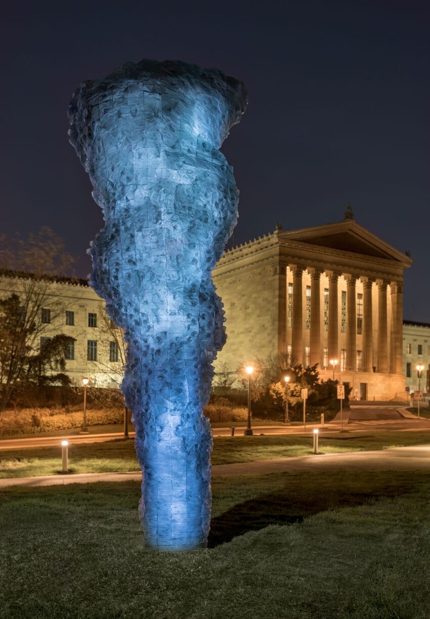 Illuminated blue outdoor sculpture near a historic building at night.
