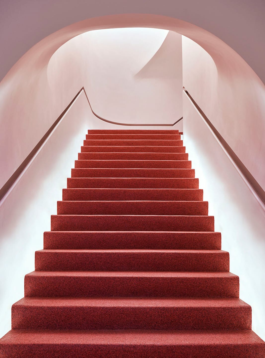 Red carpeted staircase with curved white walls and soft lighting in a modern architectural setting